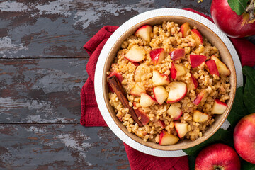Baked bulgur with apple, honey and cinnamon in a bowl on a dark wooden background top view. Sweet bulgur porridge. Tasty breakfast, vegan food.