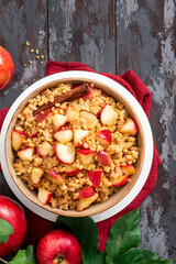 Baked bulgur with apple, honey and cinnamon in a bowl on a dark wooden background top view. Sweet bulgur porridge. Tasty breakfast, vegan food.