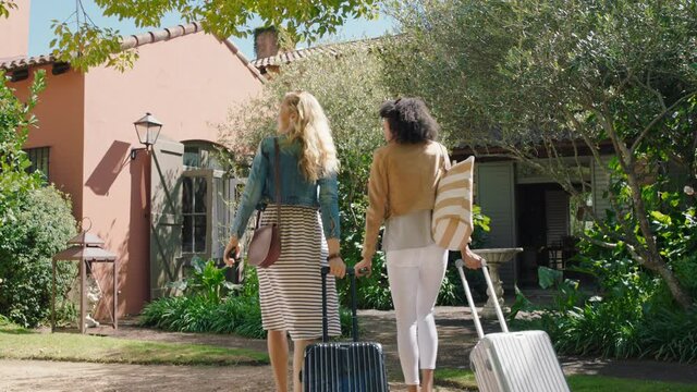 two woman friends arriving at hotel villa with trolly bags enjoying summer vacation looking at beautiful country house excited for holiday 4k footage