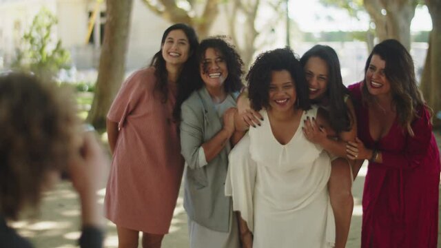 Female couple having fun and taking wedding photo with friends. Afro-American bride lifting her girlfriend on back, laughing, posing and mugging for camera. Photoshoot, LGBT wedding concept