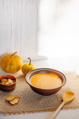 Pumpkin soup in ceramic bowl on white wooden background.