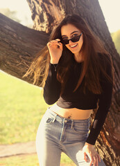 Beautiful toothy smiling teen woman looking happy in fashion sunglasses outdoors summer green trees background. Closeup portrait