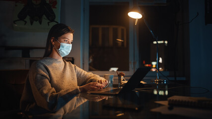Female Manager in Protective Face Mask Works on Laptop Computer in Creative Agency in Loft Office in the Evening. Renovated Stylish Design with House Plants.