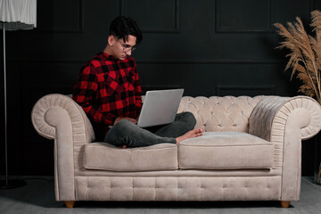 An intelligent and handsome student learns remotely at home while lying on the couch. Online lecture on laptop. The copywriter works outside the office.