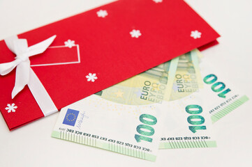 Christmas theme Envelope with white ribbon and money inside. Bunch of Euro's. One hundred (100) euro denomination. Close-up.