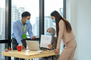Group of diverse corporate colleagues wearing protective medical face mask for health, working with computer laptop in office. Muslim woman in medical face mask working her colleagues in office