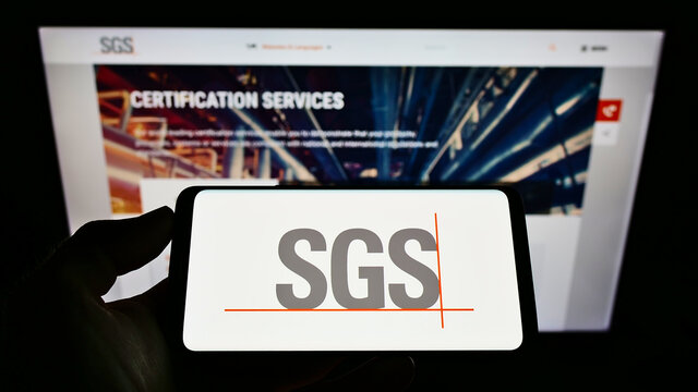 STUTTGART, GERMANY - Jun 20, 2021: Person holding cellphone with logo of certification company SGS S.A. on screen in front of webpage.