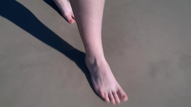 Bare feet walking across wet sand into the waves