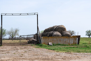 Haystacks piled up behind a fence in the middle of a field. Driveway, gate and car seat in front