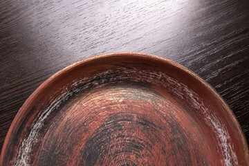 Used earthenware plate (pot tray). Selective focus. Scuff marks. Dark wood textured background