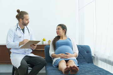 Cheerful Caucasian pregnant woman lying down on sofa and consulting to male doctor