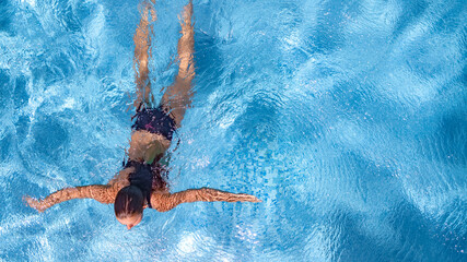 Active young girl in swimming pool aerial drone view from above, young woman swims in blue water...