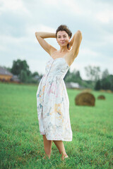Fototapeta na wymiar Portrait of a girl with short black hair in a bright white dress amongst haystacks in a green field.