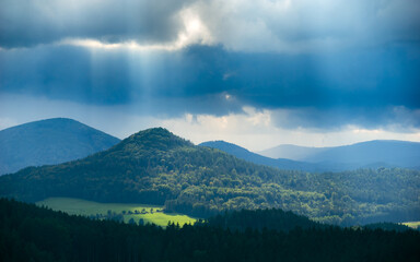 scenic view of mount Sokol in sunshine under heavy dark storm clouds as seen from mount "Popova skala" in the Czech republic 