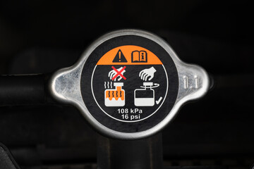 the metal cover of a radiator cap with a warning label in a car engine. A car maintenance and...