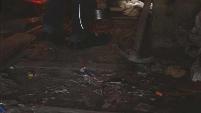Men's feet in heavy boots and jeans walk across the dusty, trash-laden attic. An axe in his hand. A pickaxe stands in the background. The concept of a homicidal maniac