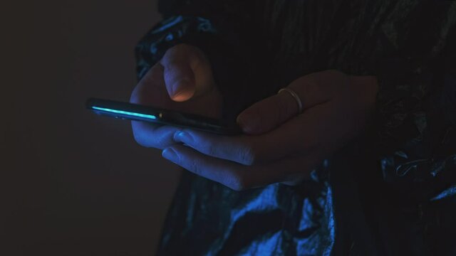 Hands in neon dark lighting using a mobile phone to scroll and typing a message. Concept hacker cracks code or password.