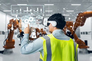 Behind Asian man engineer worker wearing VR headset working control robotic  industrial in factory....