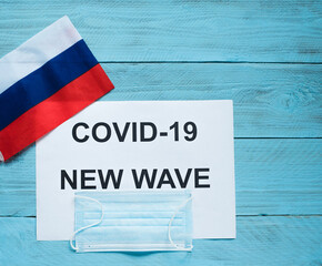On a blue wooden background there is a sheet with the inscription: covid -19 new wave, a medical...