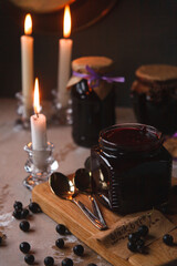 Glass jars with black currant jam in dark vintage interior with burning candles
