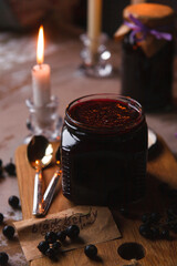 Glass jars with black currant jam in dark vintage interior with burning candles