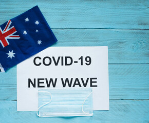 On a blue wooden background is a sheet with the inscription: covid -19 new wave, a medical mask and...