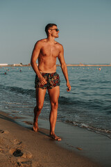 Fototapeta na wymiar Handsome muscular man walking out of the water on a turquoise water beach.