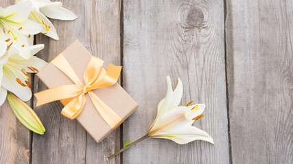 Gift box and bouquet of white lilies on wooden background