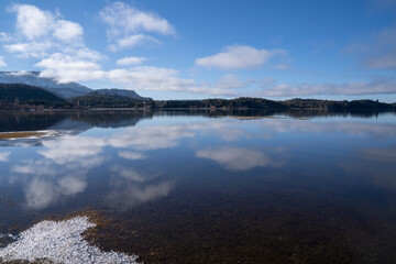 The calm lake in a sunny morning. Panorama view of the forest, lake and the perfect reflection of the sky in the blue water. The Andes mountain range in the background.