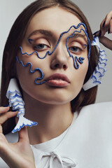 Portrait of woman in wire mask and with blue and white fish earrings