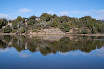 Panorama view of the wooden lake houses in the forest. The shoreline, wood, cliffs, and blue sky reflection in the water.
