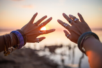 Female hands touch the sun. Hippie woman hands with silver rings at sunset. Indie boho vibes and...