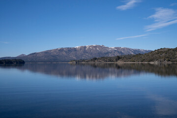 The lake in a sunny morning. Panorama view of the forest, lake and the perfect reflection of the sky in the blue water. The Andes mountain range in the background.