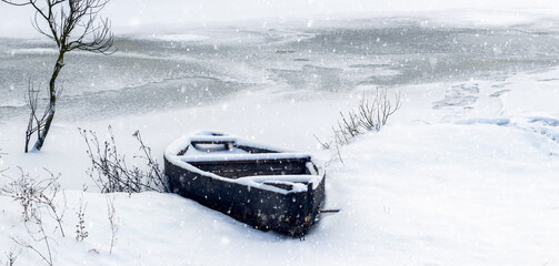 Snow-covered boat on the river in winter during a snowfall