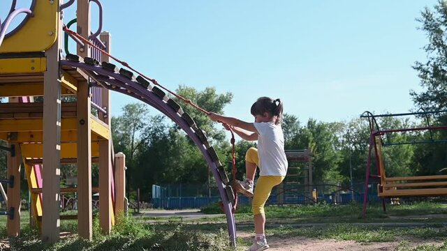 the girl climbs on the children's playground in the early summer morning on the playground.