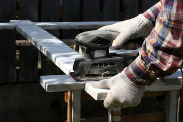 A man with an electric vibration sander treats the surface of a board