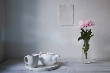 Scandinavian style. Interior Design. Large pink chrysanthemum in a long glass vase. Cup and tea pot on the tray. Empty space for text