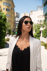 Close up image of happy brunette woman in sunglasses and summer clothes posing sideways outdoors