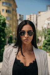 Close up image of happy brunette woman in sunglasses and summer clothes posing sideways outdoors