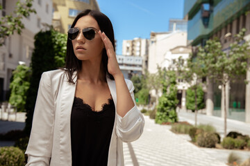 Close up image of happy brunette woman in sunglasses and summer clothes posing sideways outdoors