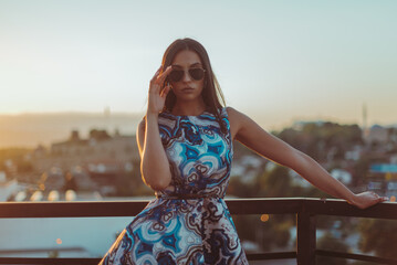 Close up image of happy brunette woman in sunglasses and summer clothes posing sideways outdoors