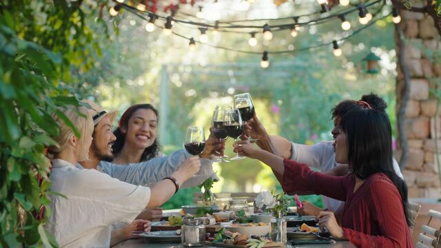 friends making toast celebrating dinner party drinking wine eating mediterranean food sitting at table enjoying beautiful summer day outdoors 4k footage 