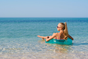 Happy girl with long hair floats on an inflatable ring in the sea. View from the back.