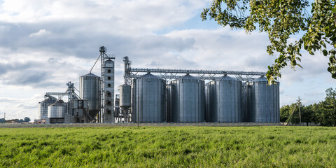 Fototapeta na wymiar Silver silos on agro-processing and manufacturing plant for processing drying cleaning and storage of agricultural products, flour, cereals and grain. Modern Granary elevator and seed cleaning line.