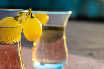 Detail of ripe grapes adorning the rim of some crystal glasses with cava or champagne, illuminated...