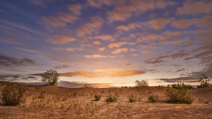 Shining bright clouds and sandy landscape with starry sky at sunrise