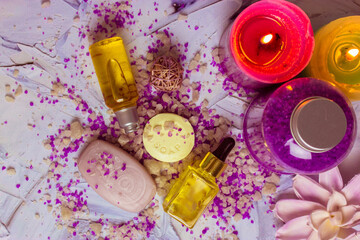 Lavender-scented sea salt crystals scattered on a table, soap bars, bottles of face body care oil, cosmetic essential serum, pink lotus flower, candles flat lay. Spa beauty day. Beautiful composition.