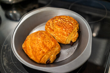 Closeup of two golden brown baked pastry croissants on baking tray pan with flaky crust and chocolate filling