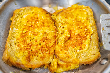 Closeup of two homemade cooked challah brioche bread french toast frying in pan as savory eggy style