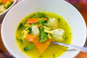 Macro closeup of Chinese traditional wonton soup bowl with carrots and snap peas as asian meal with spoon